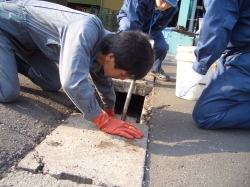 側溝に顔を近付けて掃除をしている写真